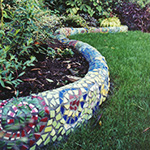 Colorful glass and tile are cut and combined into a swirling mosaic on this small curving wall set off by plants that accent the design.
