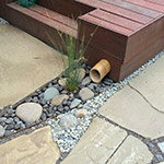 Bamboo is used as a downspout extension in this river rock spillway through a bluestone patio to the Rain Garden. Hardscape by Apogee Landscapes.